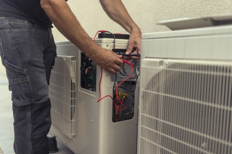 Close-up on the hands of the electrician installing the heat pump, connecting the wires.